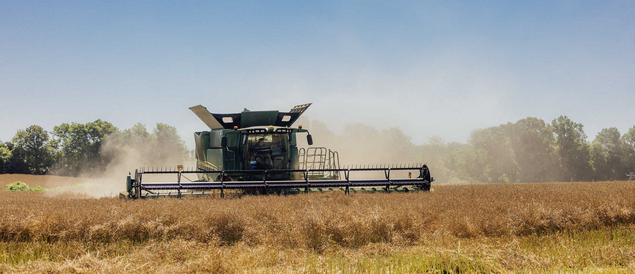 Platform header driving through a field in a cloud of dust.